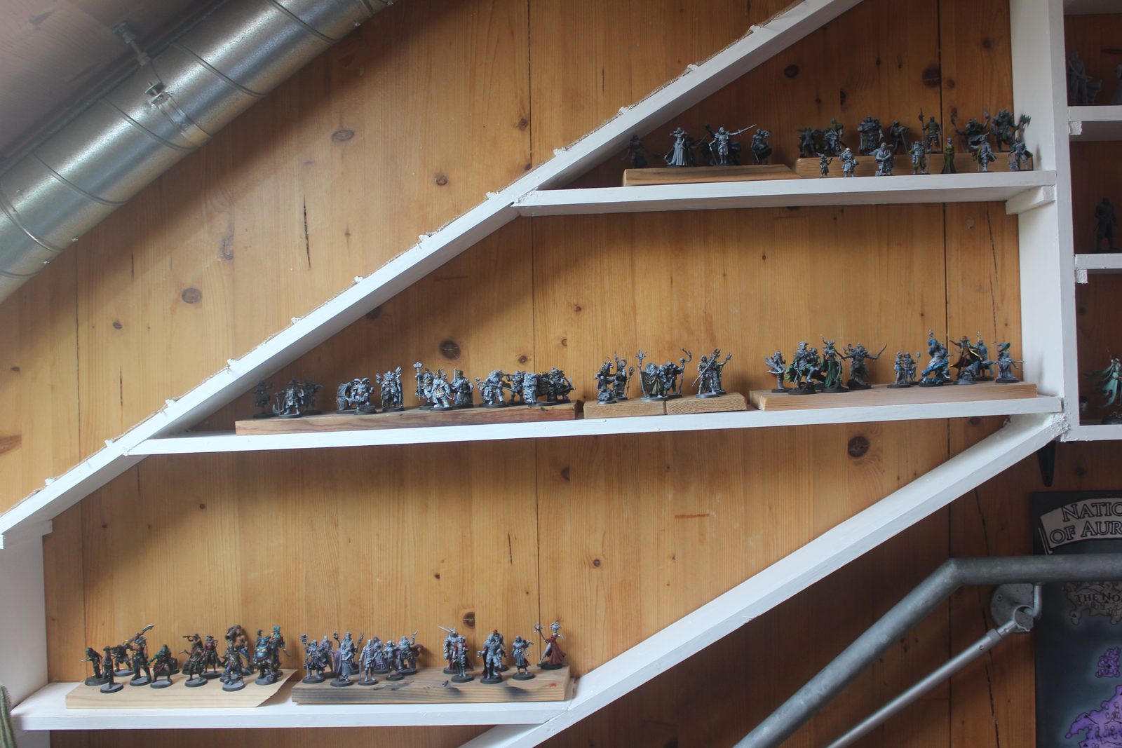 Three white triangular display shelves crowded with dozens of fantasy miniatures
